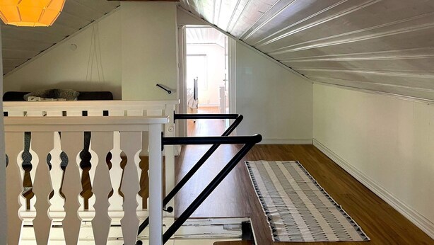 Une pièce avec un plafond en pente, un plancher en bois, une rambarde blanche et un tapis à motifs.