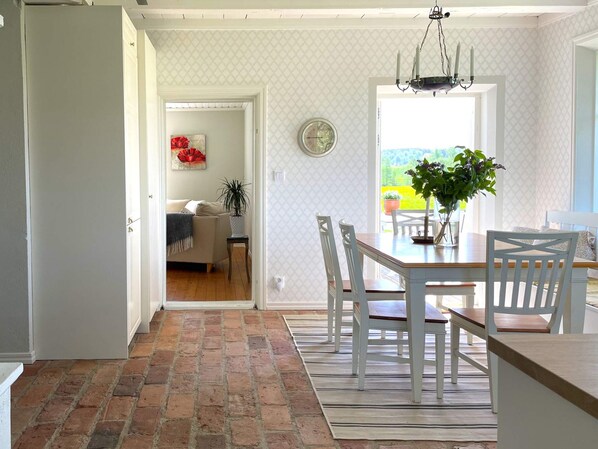 A dining area with a brick floor, white chairs, a wooden table, and a chandelier.