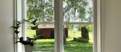 Et vindue med udsigt over et grønt landskab og en bygning med rødt tag.