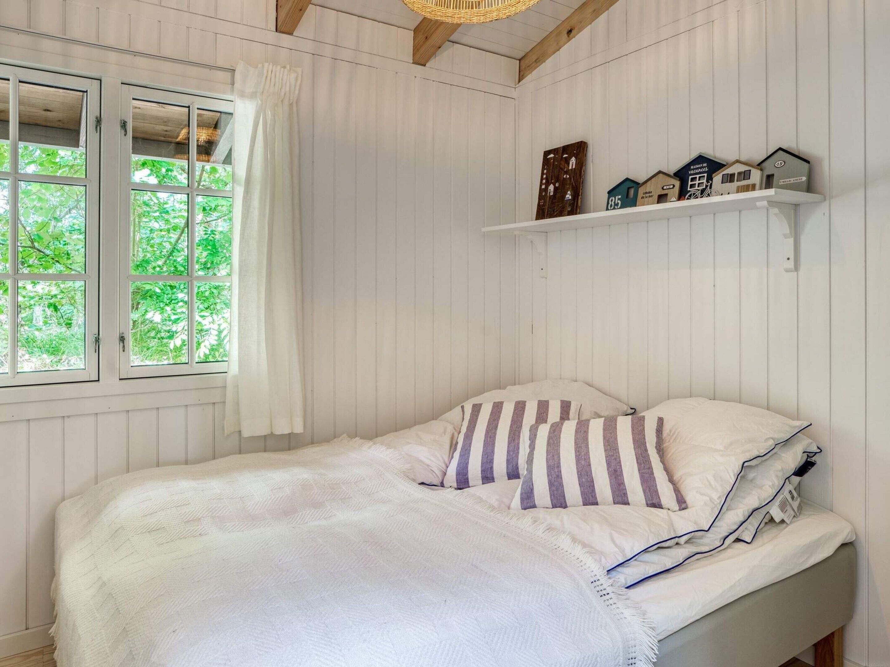 Et soveværelse med seng, et vindue med gardiner og en hylde med husformede dekorationer.