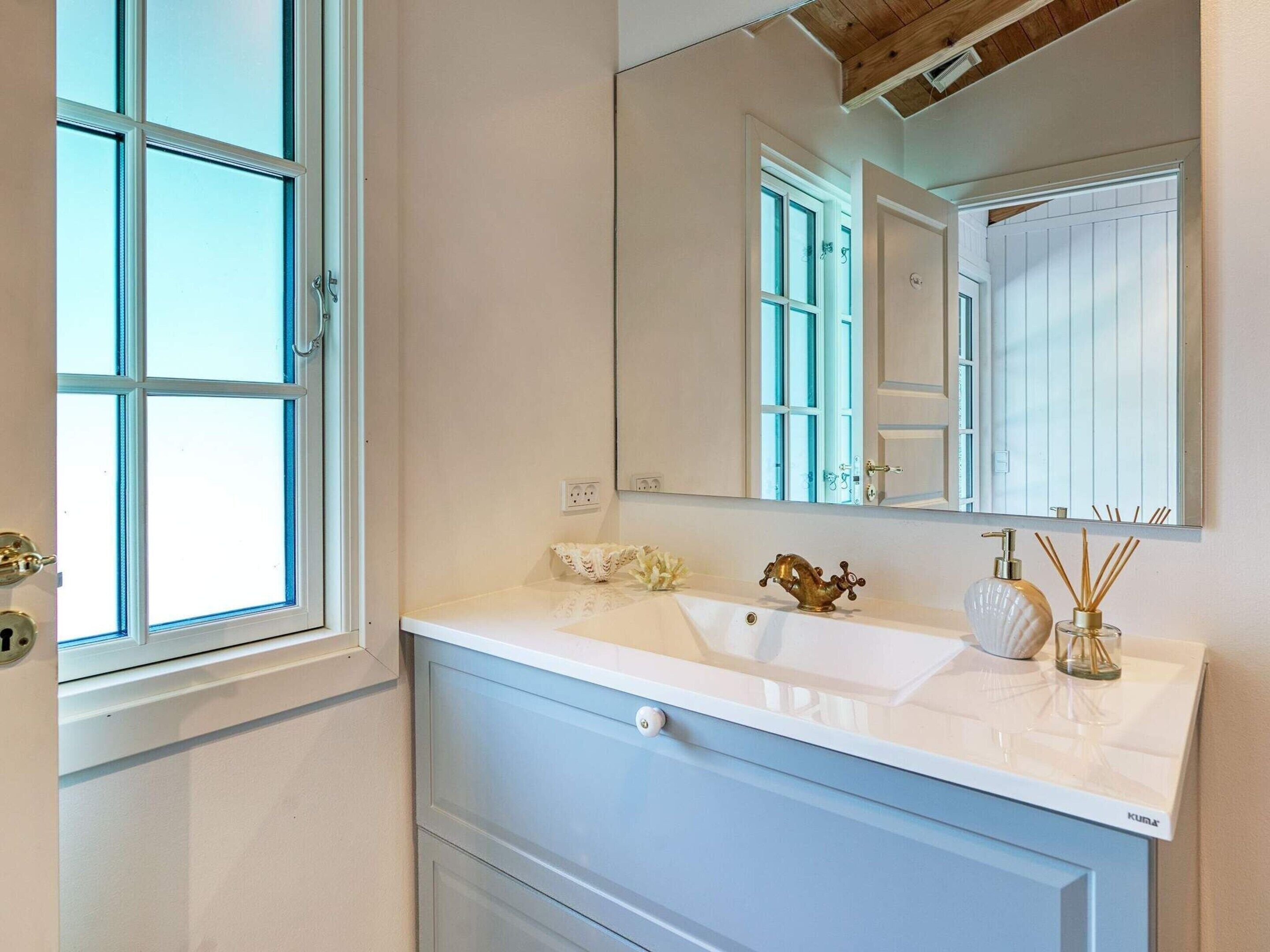 Une salle de bain avec un lavabo blanc, un miroir et une fenêtre avec des volets blancs.