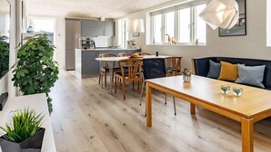 A modern kitchen with a central island, a dining area with a wooden table and chairs, and a seating area with a sofa.
