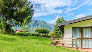 Una cabaña con terraza de madera y vista a las montañas al fondo.