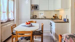 Cocina compacta con armarios blancos, microondas y una pequeña encimera con tetera y utensilios.