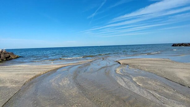 A beach with a concrete path leading to the water, a clear sky, and distant rocks. - 4 Person Holiday Home in Saeby (Sæby)