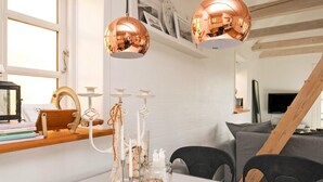 A dining area with a white table, two copper pendant lights, a glass candle holder with candles, and a rustic wooden shelf with books and a clock. - 4 Person Holiday Home in Saeby (Sæby)