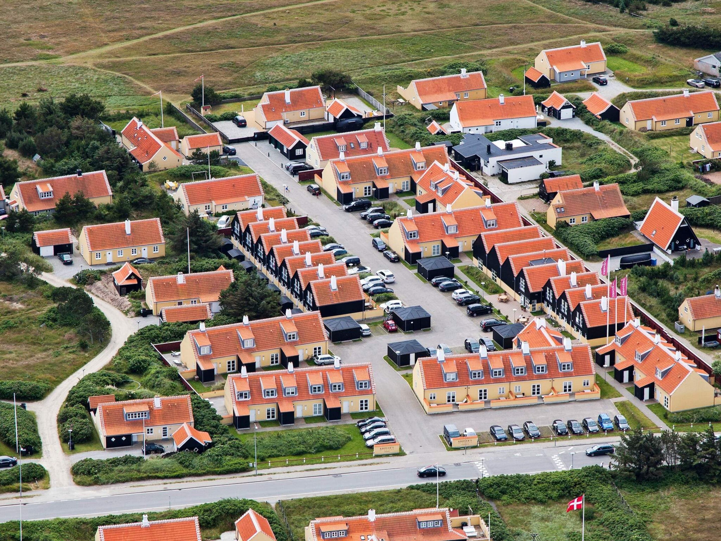 A residential area with uniform houses, a main road, and parked cars.