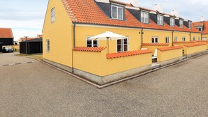 Une rangée de bâtiments jaunes aux toits orange, une allée gravillonnée et un parasol blanc.
