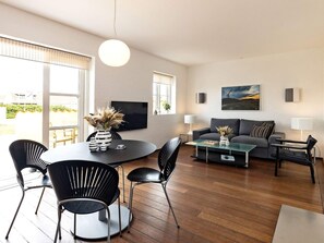 Una sala moderna con una mesa de comedor redonda, sillas negras, un sofá gris y un televisor de pantalla plana montado en la pared.