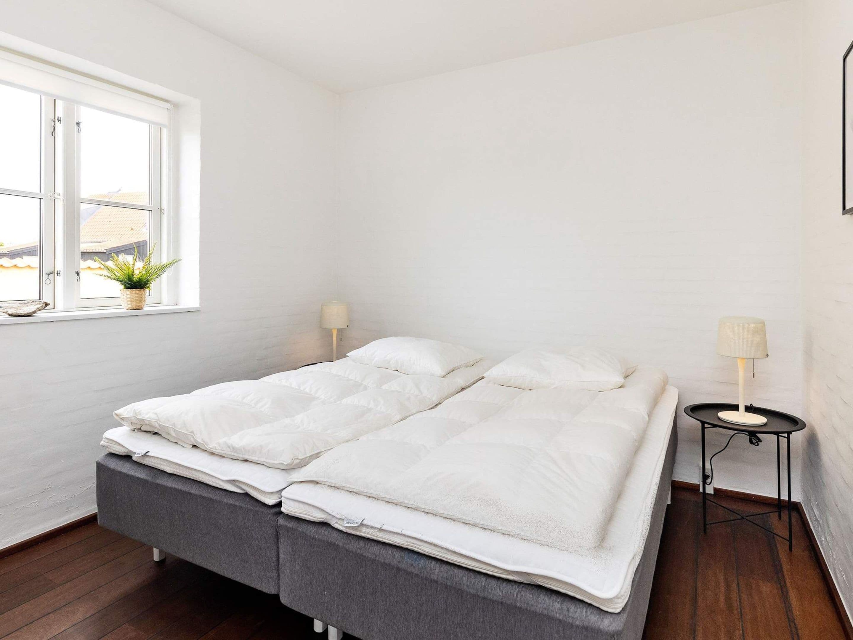 A minimalist bedroom with a bed, bedside lamps, and a window with a plant.