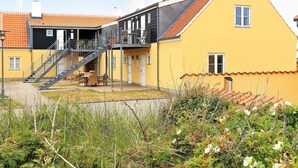 A yellow building with a staircase leading to a balcony, surrounded by vegetation. - 5 Star Holiday Home in Skagen (Skagen)
