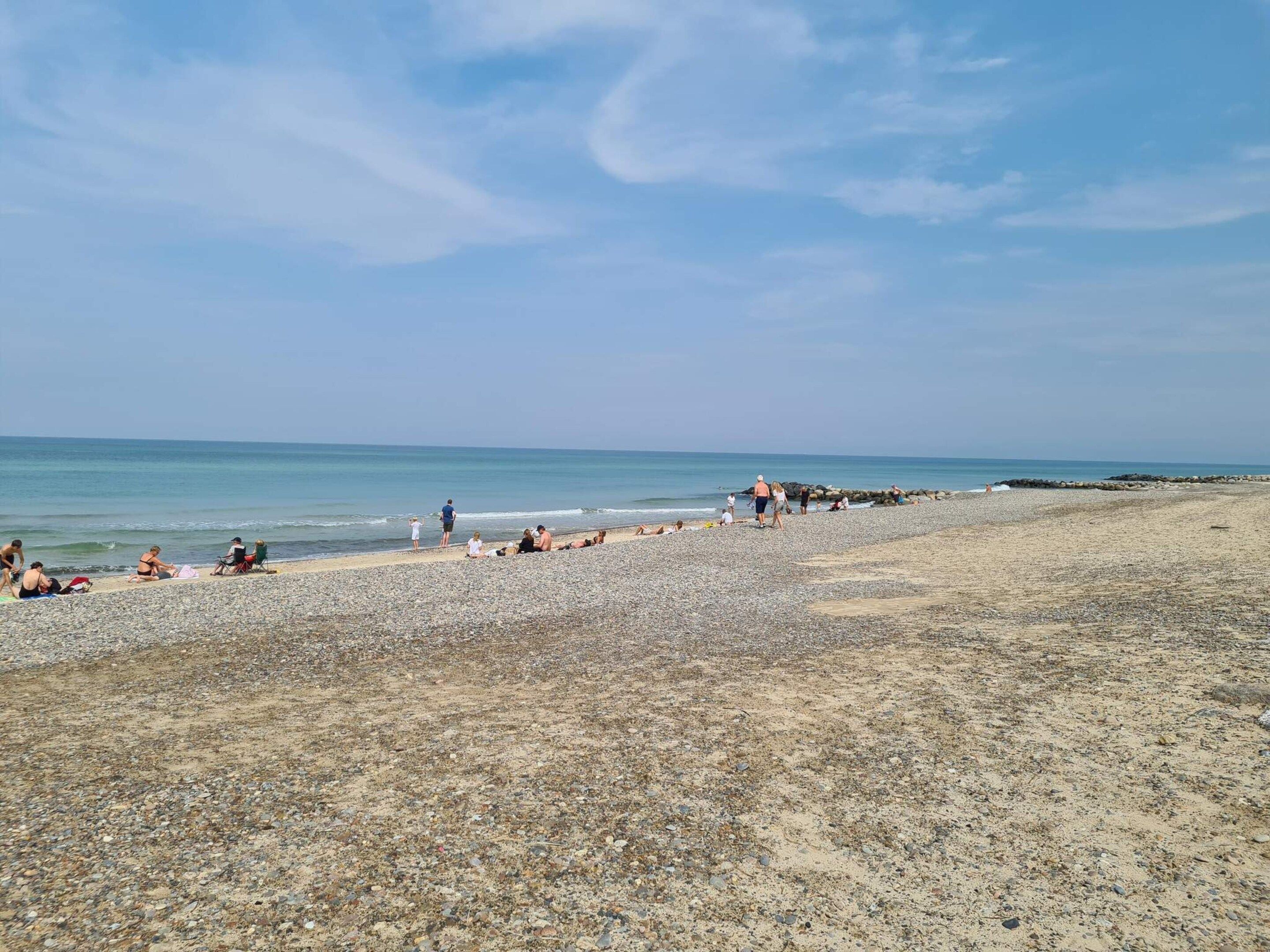A pebbly beach with people relaxing and walking along the shore.
