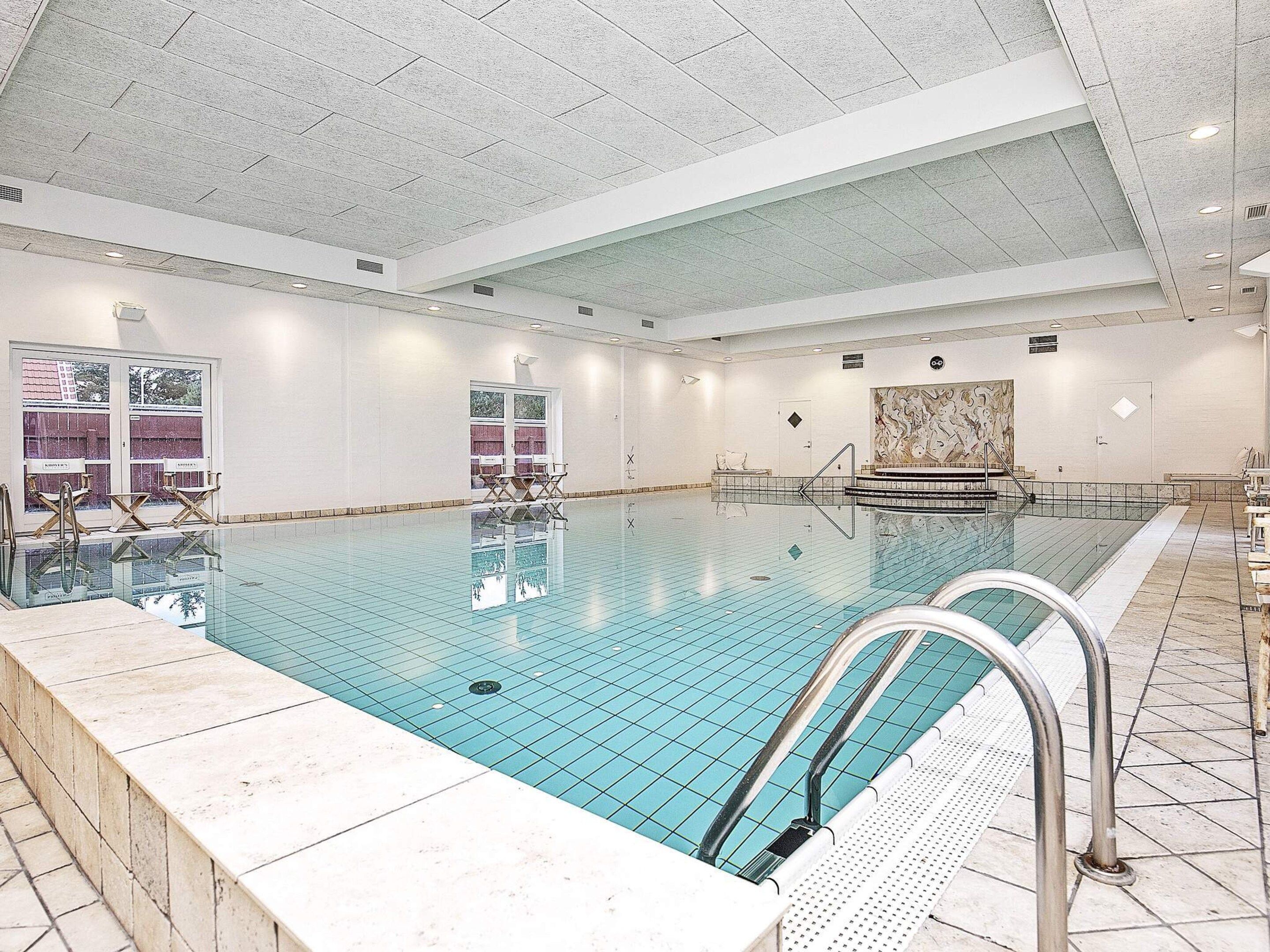 Una amplia piscina cubierta con agua cristalina, rodeada de paredes blancas y suelo de baldosas.