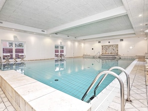 A large indoor swimming pool with clear water, surrounded by white walls and a tiled floor.