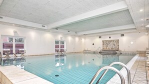 Suuri sisäuima-allas, jossa on kirkasta vettä, ja sen ympärillä on laatoitetut seinät sekä korkea katto.