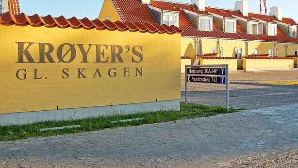 A yellow building with "KROYER'S GL. SKAGEN" signage, a gravel driveway, and a signpost with directions to "Højensvej 30A-34P" and "Vandrestien 7-12". - 5 Star Holiday Home in Skagen (Skagen)