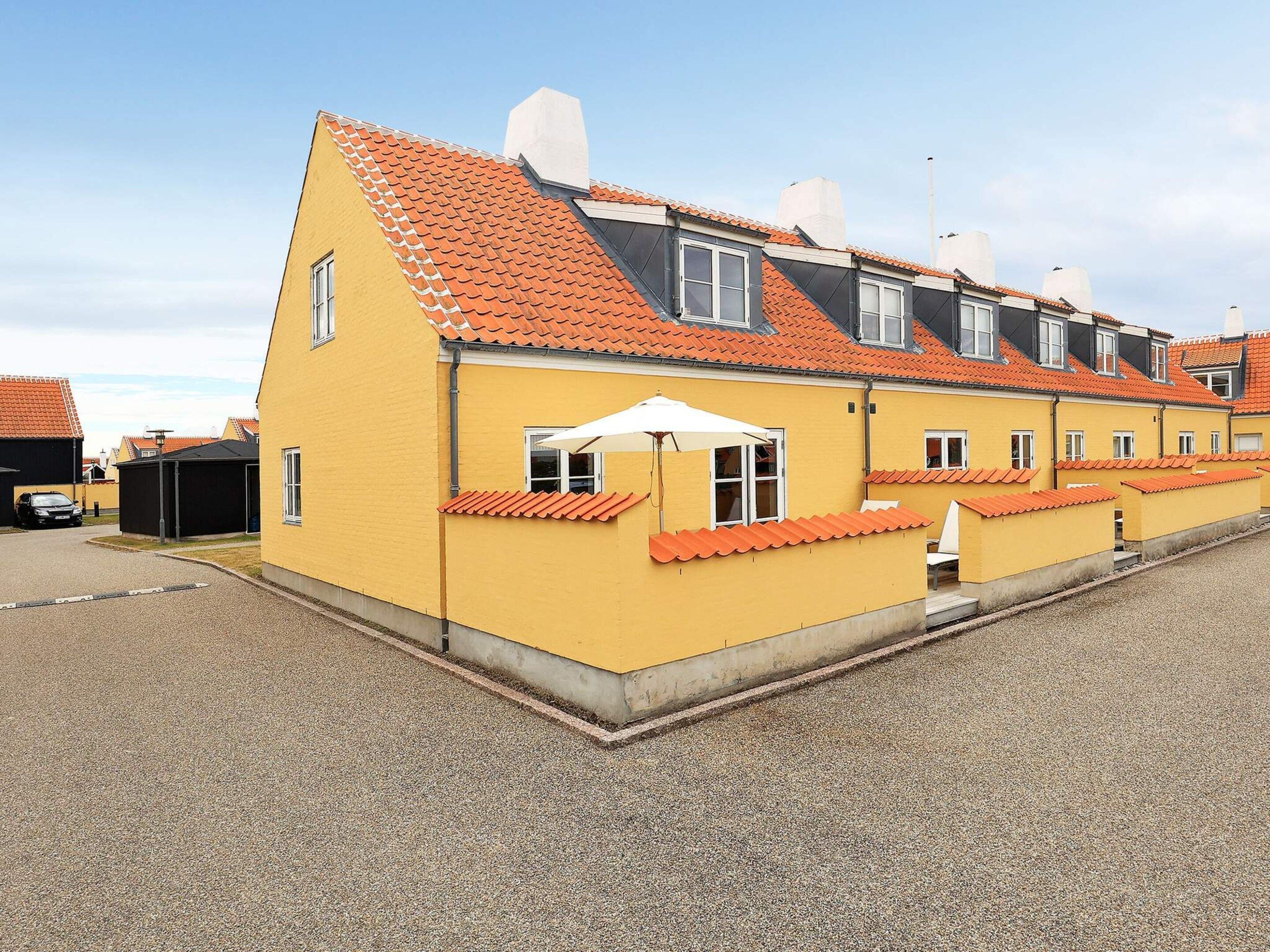 A row of yellow buildings with orange roofs, a gravel driveway, and a white umbrella.