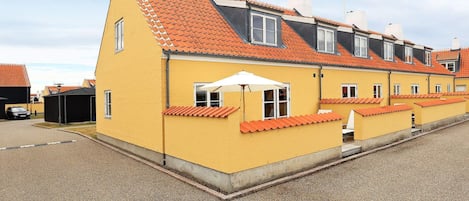 A row of yellow buildings with orange roofs, a gravel driveway, and a white umbrella.