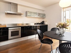 A modern kitchen with a built-in oven, a stainless steel range hood, and a dining area with a round table and black chairs.