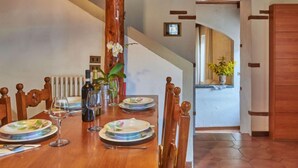 A dining room with a wooden table set for four, a clock on the wall, and a staircase leading to another room. - Casa Rosy by Interhome (Porlezza)
