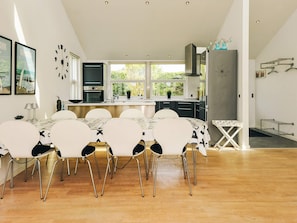 A modern kitchen with a central island, white dining chairs, and a wooden floor.