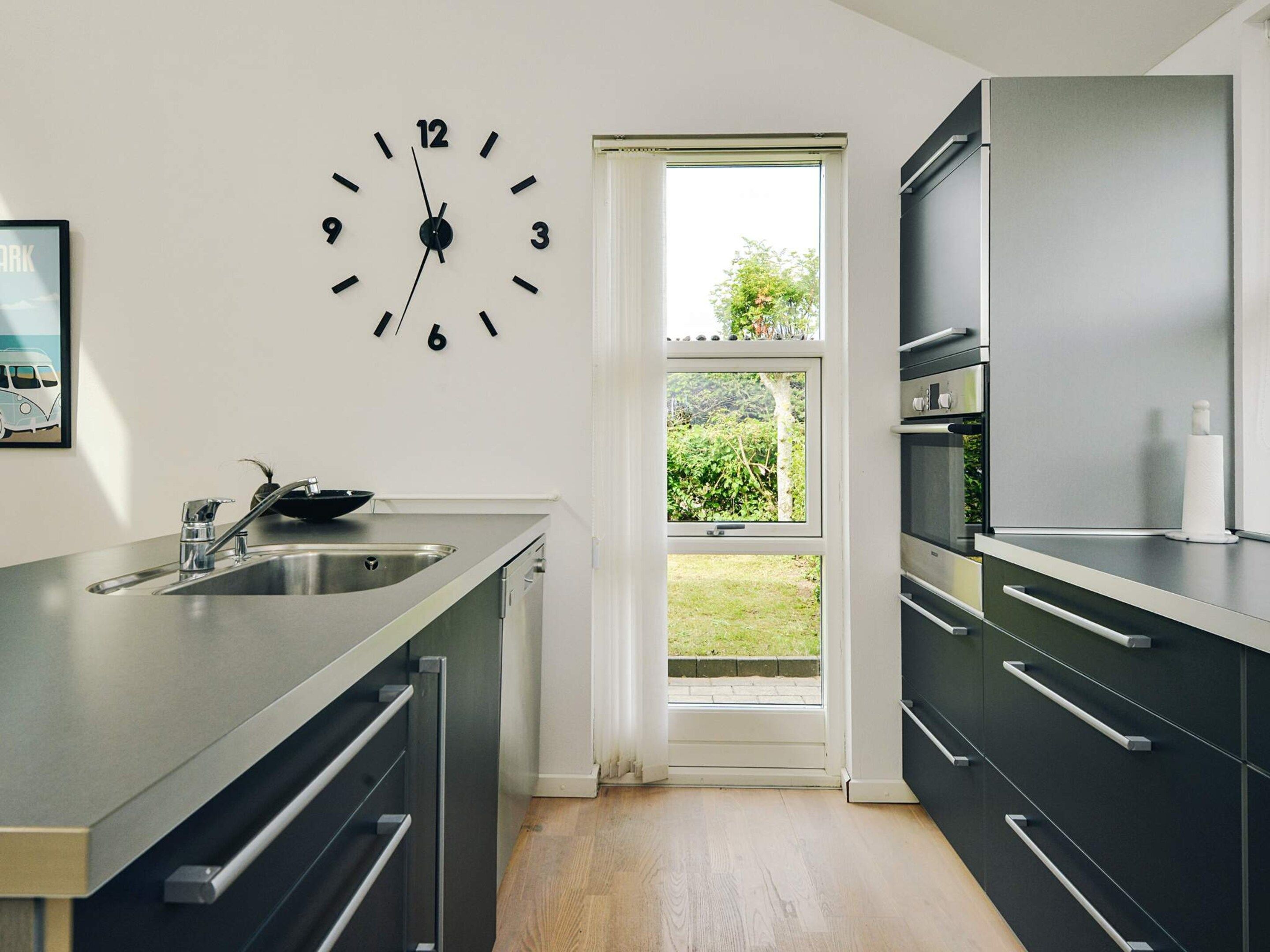 A modern kitchen with a built-in sink, a wall clock, and a window leading to a garden.