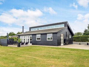 A modern two-story house with a flat roof, large windows, and a well-maintained lawn.