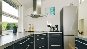 Eine moderne Küche mit dunklen Schränken, einem Edelstahlkühlschrank und einem Fenster mit Blick auf Grünfläche.