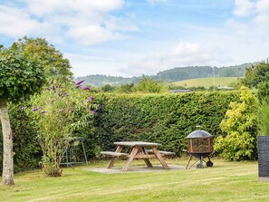 A picnic area with a wooden table and benches, surrounded by lush greenery and a view of rolling hills.