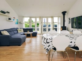 A modern living room with a dark blue sofa, a round coffee table, and a dining area with white chairs and a table covered with a black and white abstract tablecloth.