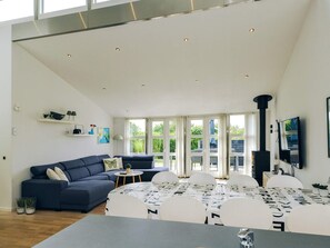 A modern living room with a sofa, dining table, and chairs. There is a fireplace and a TV mounted on the wall.