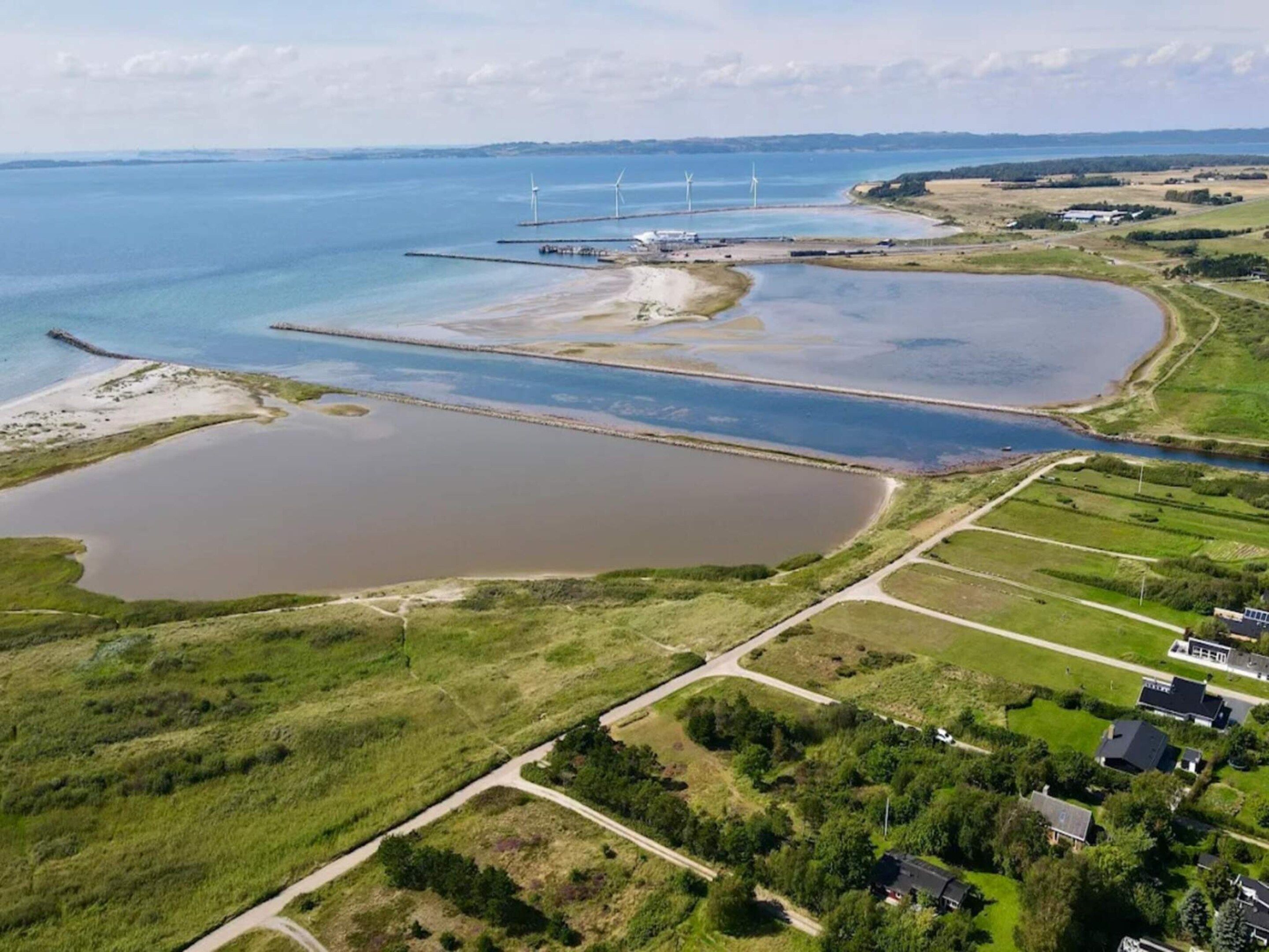 An aerial view of a coastal area with wind turbines, a marina, and residential buildings.