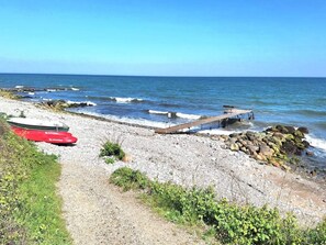 A rocky beach with a wooden pier extending into the sea, a red boat, and a small green boat.