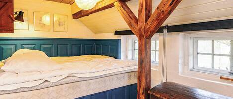 Quarto com cama, vigas de madeira, janela e luminárias fixadas na parede.