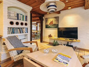 A cozy living room with a bookshelf, a TV, a dining area, and a painting on the wall.