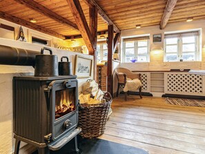 A cozy room with a wood-burning stove, a wicker basket filled with firewood, and a chair with a fluffy throw.