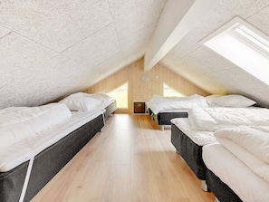 Et værelse med to senge, trægulv og et skråt loft med ovenlysvinduer.