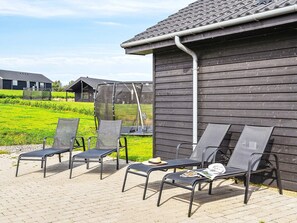 En terrasse med fire liggestole, et lille bord og et grillområde.