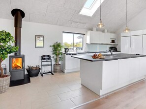 A modern kitchen with a central island, a wood-burning stove, and a view of the outdoors.