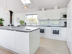 Une cuisine moderne avec des meubles blancs, un grand îlot central, des appareils en acier inoxydable et des luminaires suspendus.