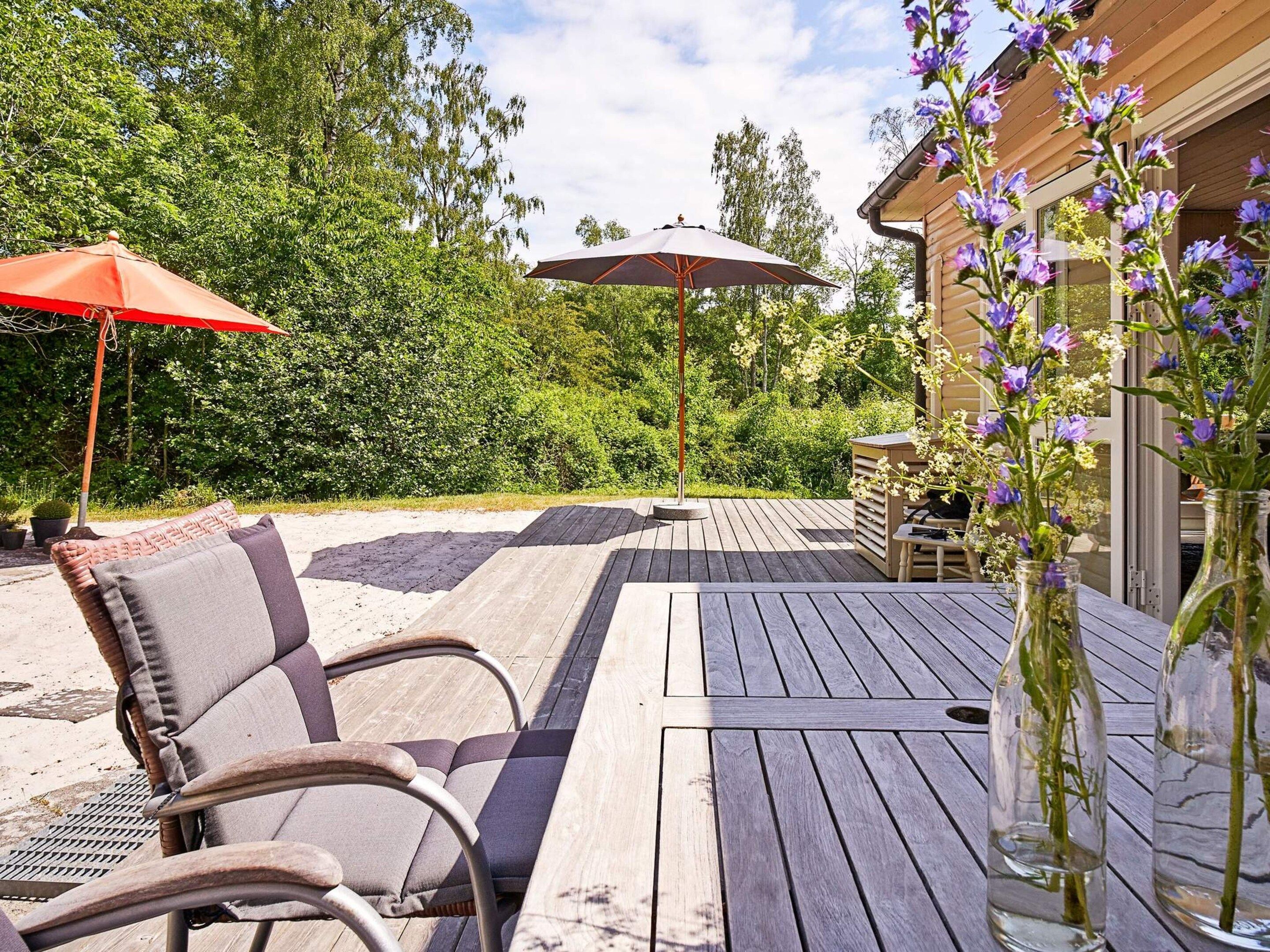 Une terrasse extérieure avec un plancher en bois, deux chaises, une table et deux parasols.