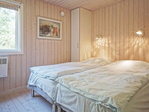 Une chambre avec deux lits, des murs en bois, une fenêtre, un tableau et des lampes fixées au mur.