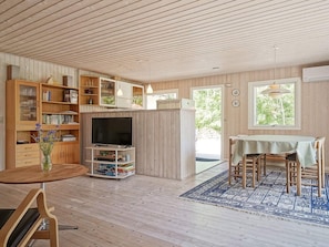 A wooden interior with a dining area, a television on a stand, and a bookshelf.