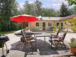 Une terrasse avec des meubles d’extérieur, un barbecue et un parasol rouge.