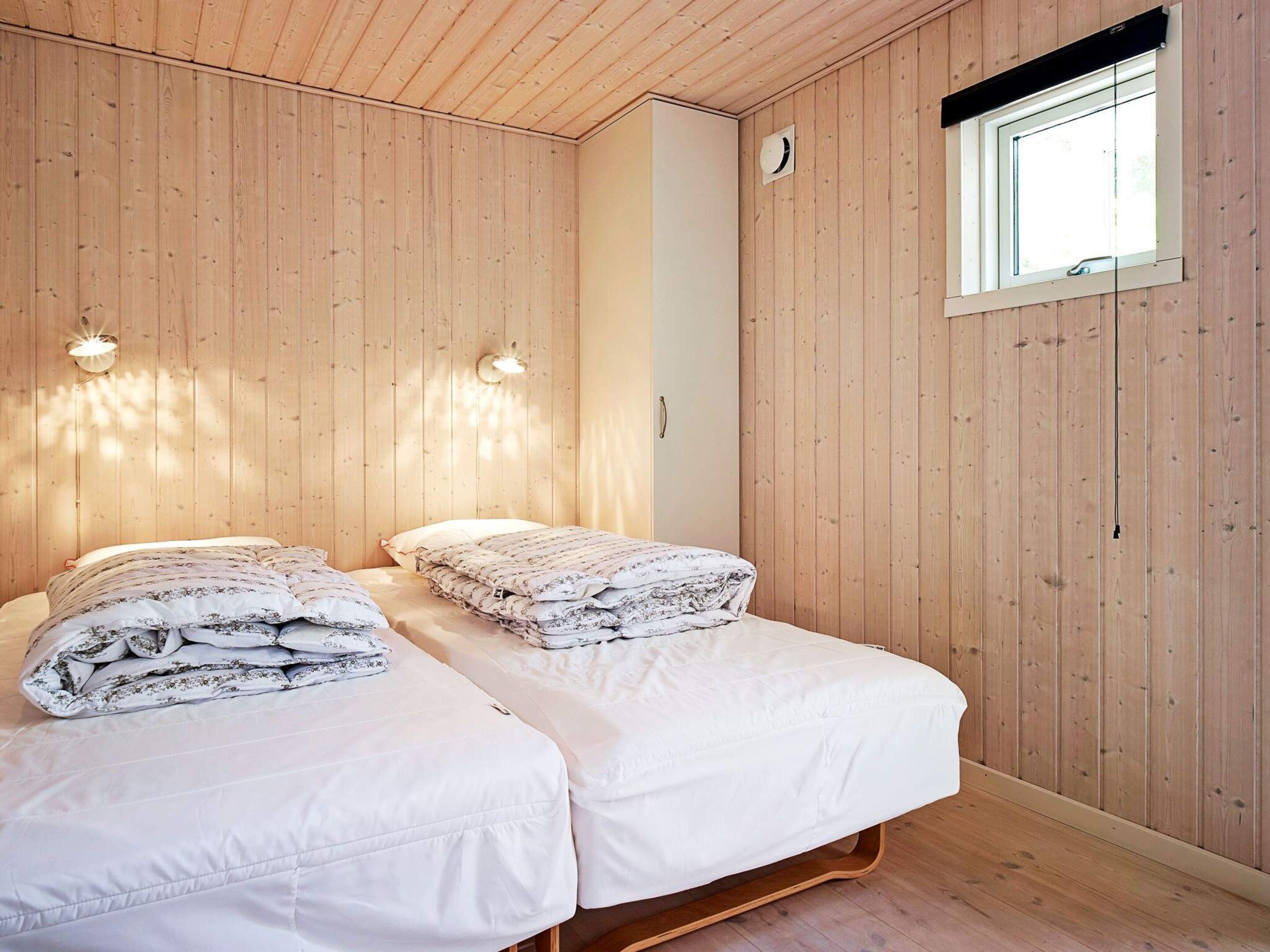 A room with two beds, wooden walls, a window, and wall-mounted lights.