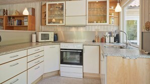 A compact kitchen with white cabinetry, a built-in oven, a microwave, and a sink. - 4 Star Holiday Home in Nexo (Nexø)