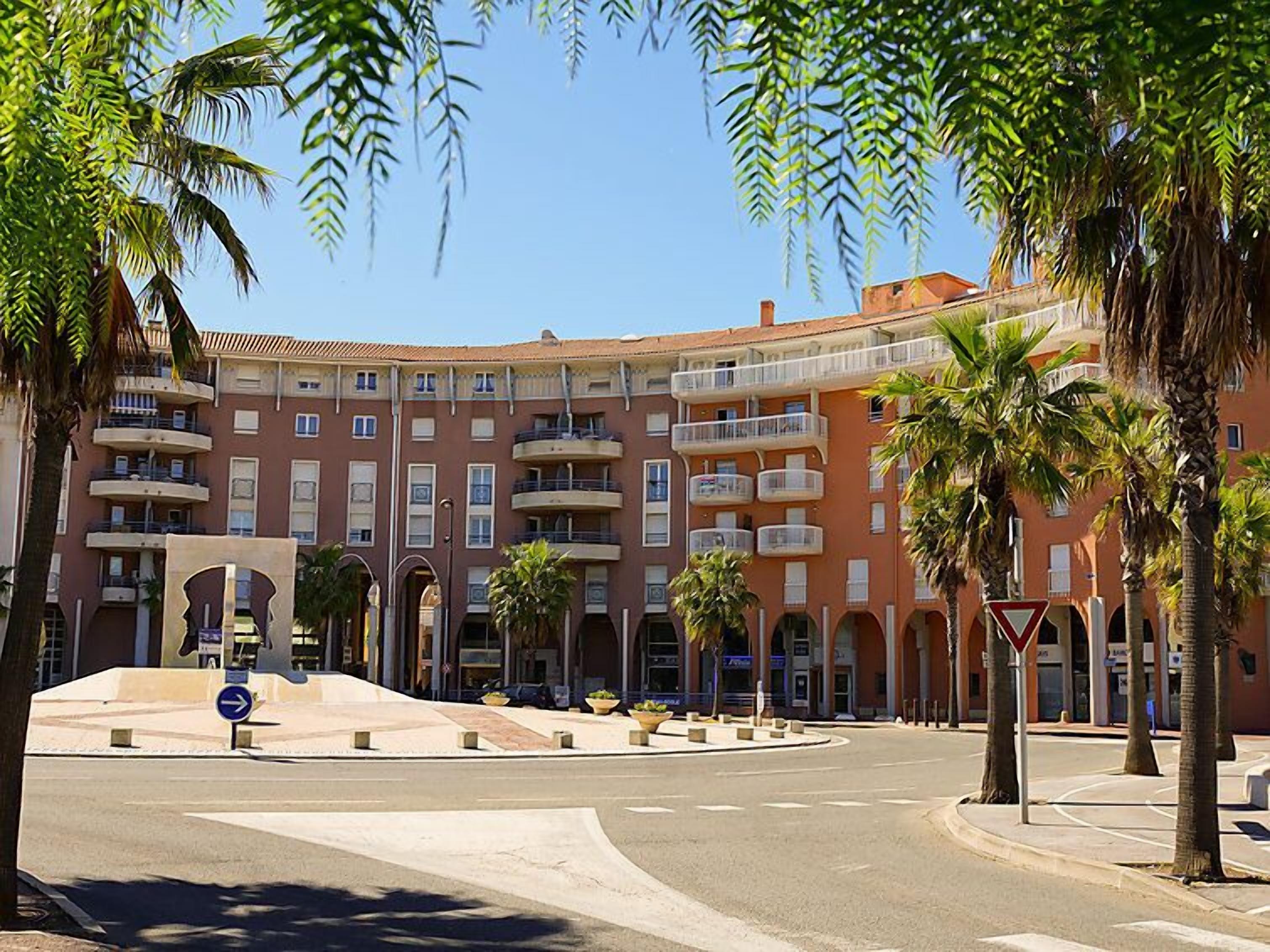 A multi-story hotel with balconies, a roundabout, and palm trees.
