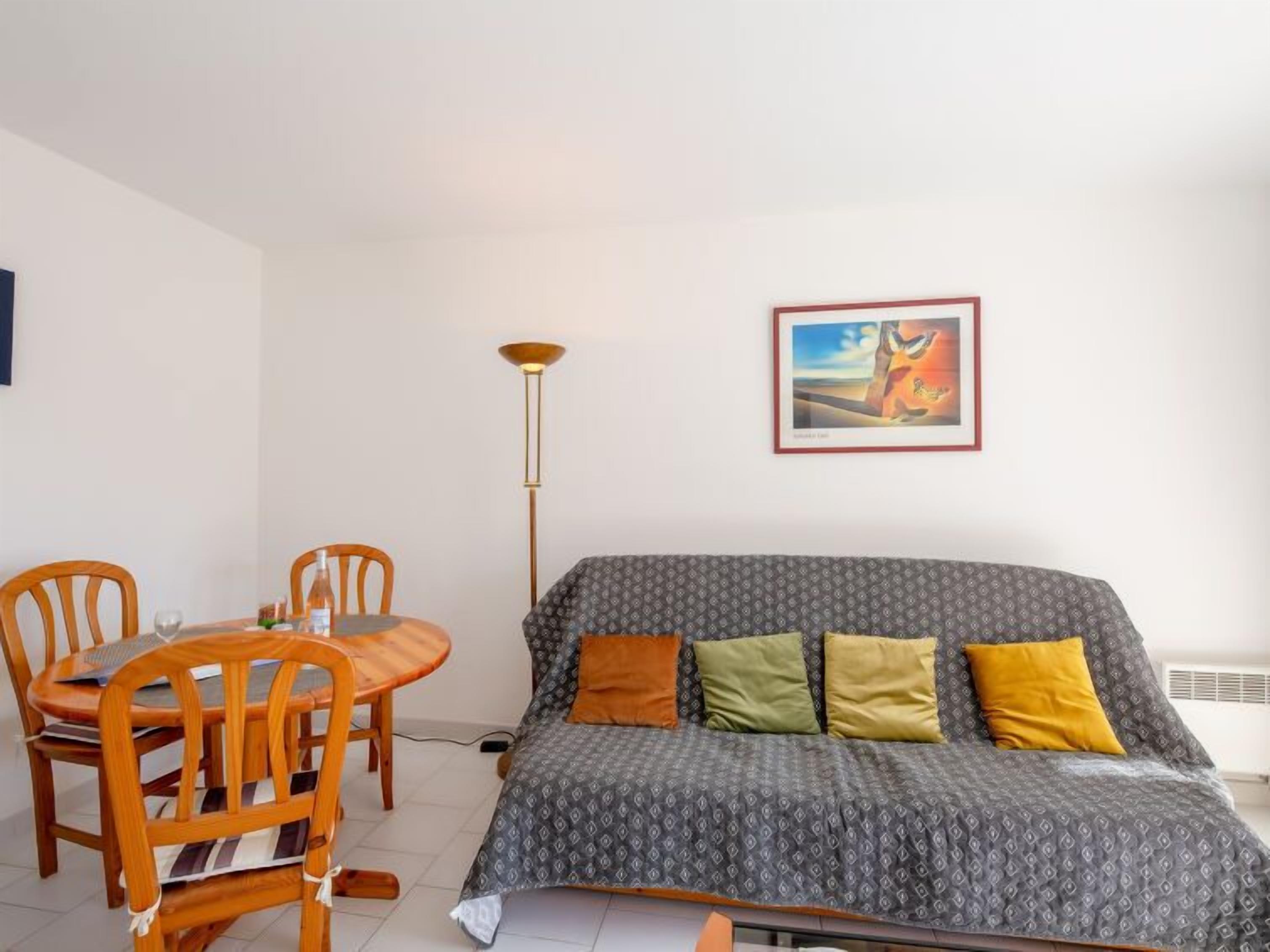 A small, furnished room with a sofa, a dining table, and chairs.