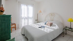 Una camera da letto con un letto, un comodino, una lampada, una sedia e una finestra con tende.