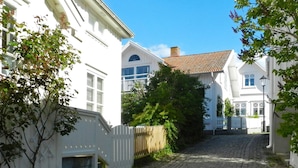 A cobblestone street flanked by white buildings with traditional architecture, including a visible wooden fence and lush greenery. - 5 Person Holiday Home in Fiskebackskil-by Traum (Fiskebackskil)